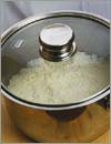 Положить рис в кастрюлю, залить его стаканом холодной воды, закрыть крышкой и поставить на сильный огонь.