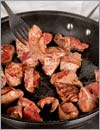 Небольшими порциями обжарить куски говядины до образования золотистой корочки, переложить их в другую посуду.